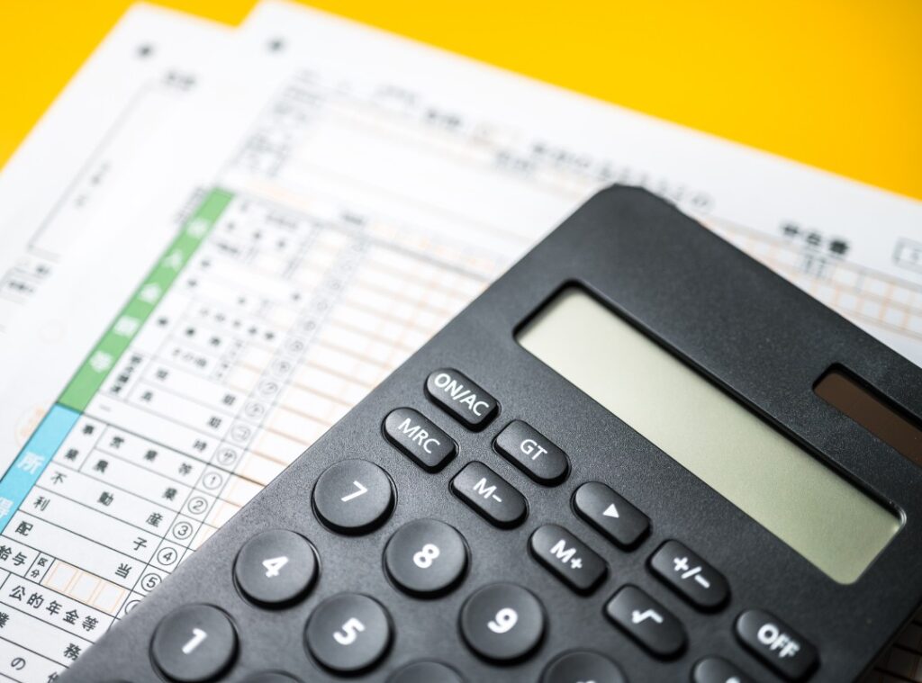 デスク上の電卓と書類。バーチャルオフィスの格安な月額料金だけでなく、入会金やオプション費用を含めたトータルコストを確認するイメージ