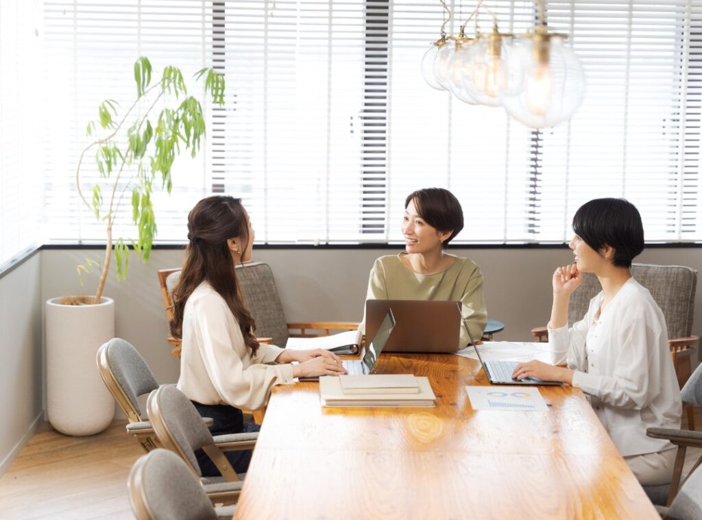 日当たりの良い開放的なワークラウンジで、リラックスしてノートパソコン作業に集中する女性。生産性を高めるリモート環境のイメージ