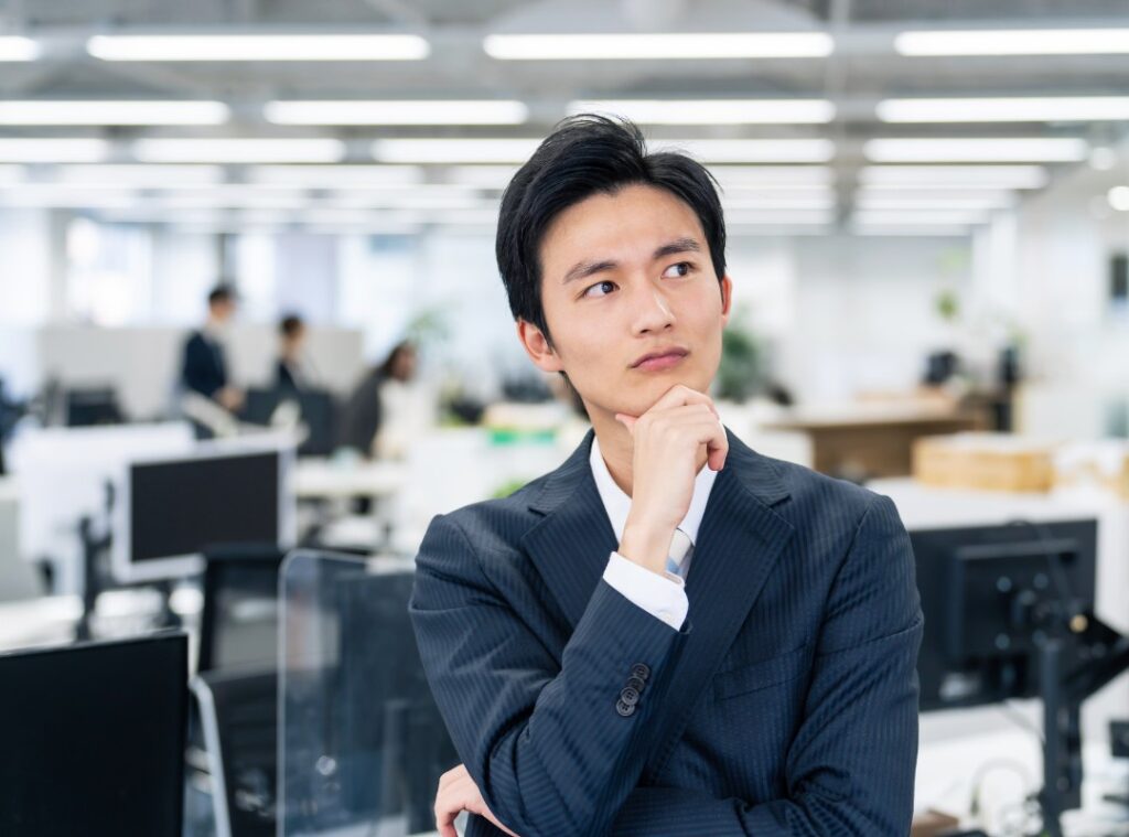 コワーキングスペースの共有デスクで、場所に縛られず多様なメンバーとコミュニケーションを取りながら働くビジネスパーソン